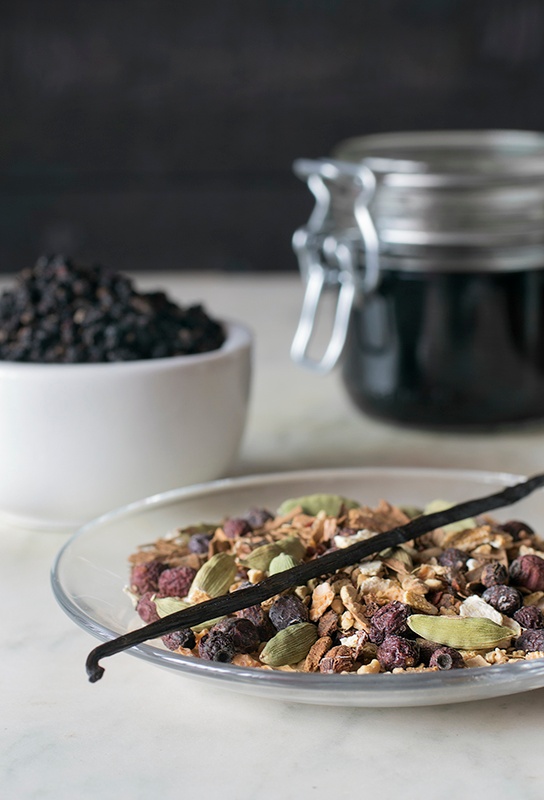 Bowl of colorful whole spices, pantry jar of elderberry syrup and displayed elder berries. 