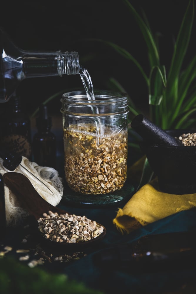 A clear alcohol is being poured into a jar of dried roots while making a tincture.