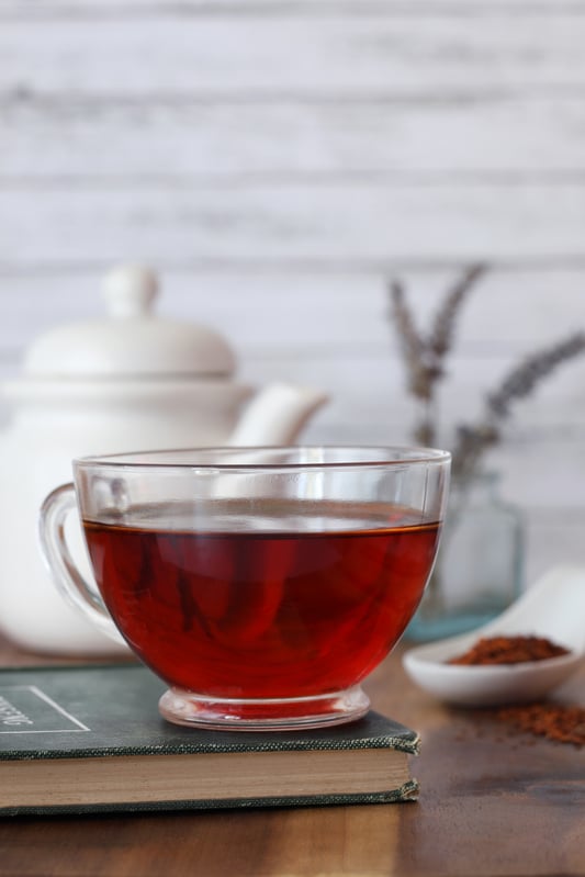 Clear crystal glass of Earl Grey Rooibos Tea sitting on book on table by teapot