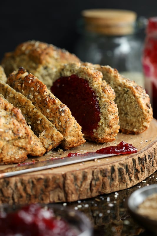 Irish soda bread on a wooden cutting board with a ruby red jam spread. Crunchy soda bread covered in nutritious seeds.