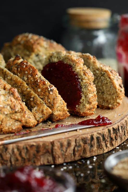 Irish soda bread on a wooden cutting board with a ruby red jam spread. Crunchy soda bread covered in nutritious seeds. 