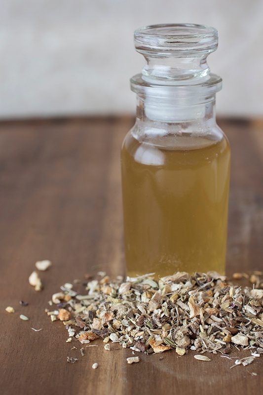 5th chakra syrup in a glass bottle with glass lid on a wood table with loose leaf tea