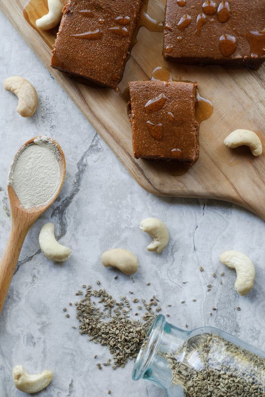 Brown homemade energy bars on a wooden board with spilled spices and cashews