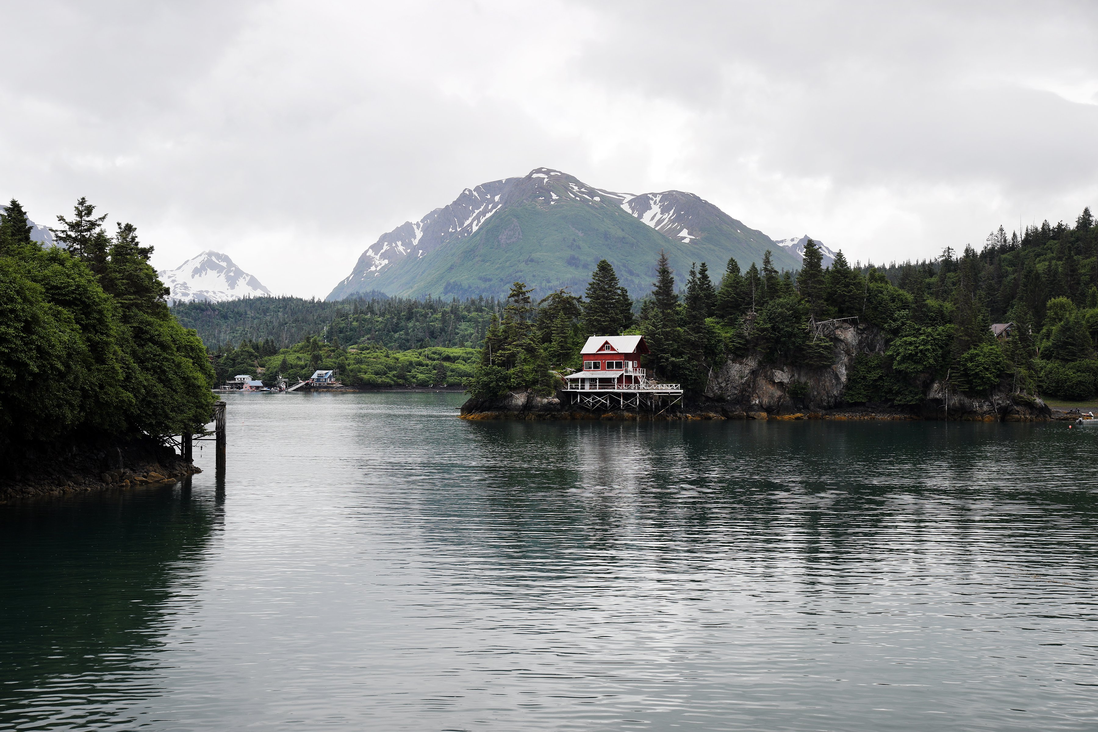 Picture of lake with snow capped mountains in background and modest water front property in Alaska. 