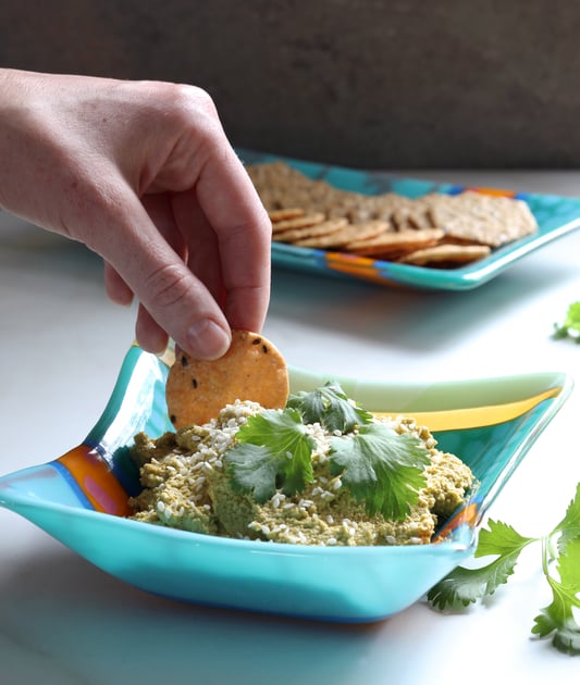 Hand reaching for dip with cracker in blue bowl