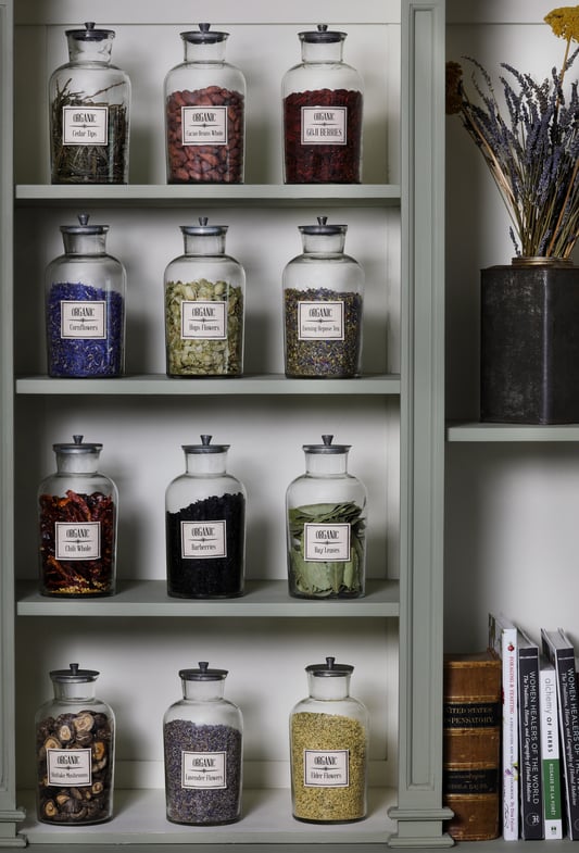 Green book case and shelving with large glass containers of dried herbs out for display