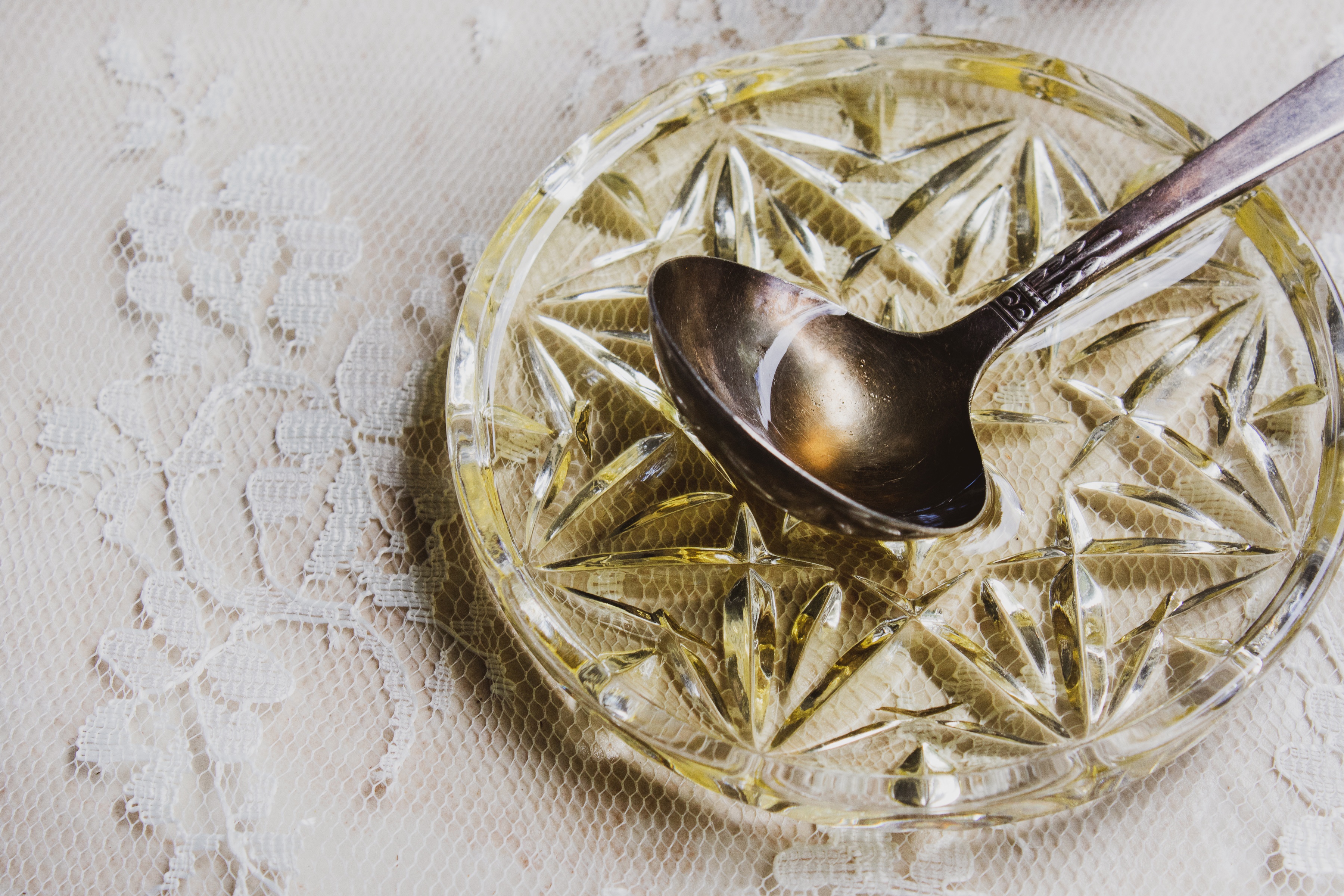 Spoon with argan oil resting on small crystal bowl with argan oil on top of lace counter