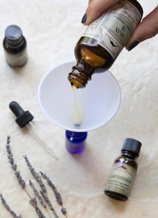 Hand pouring argan oil into funnel in order to make a recipe for hair serum