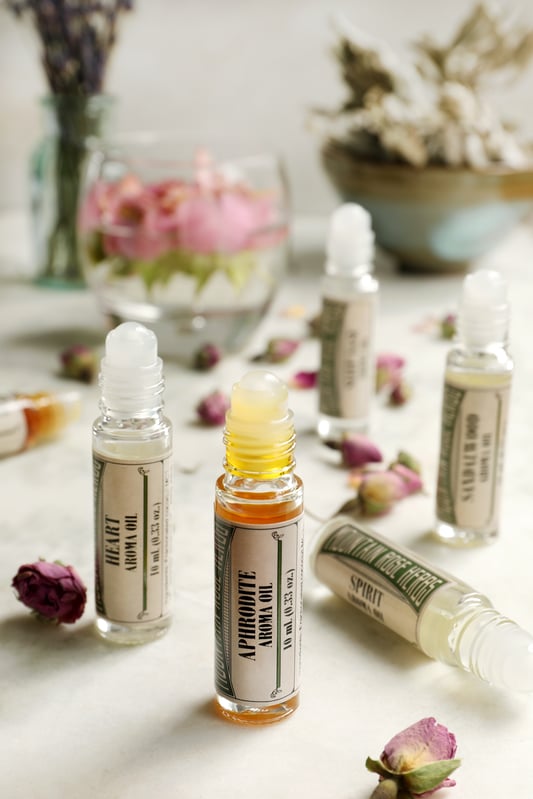 Roll-on aroma oils arranged with dried whole rose buds. Different aroma blends such as Aphrodite, Heart, and Sandalwood. 