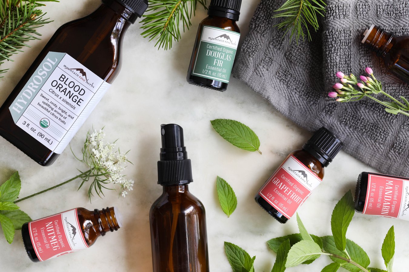 Equipment for making an aroma spray, including Blood Orange hydrosol, a spray bottle with mister, and Douglas Fir, Grapefruit, Mandarin, and Nutmeg essential oils.