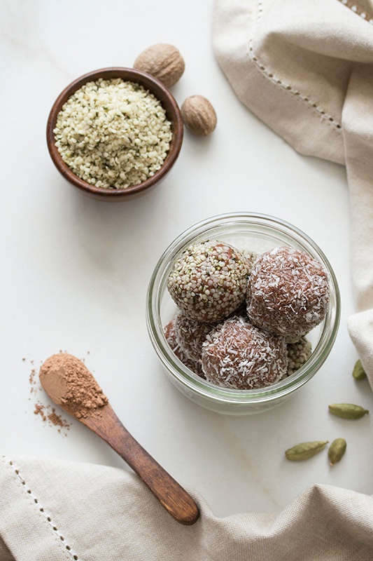 Ashwagandha Chocolate Chai bites in a glass bowl on table cloth with hempseeds and spoon of cacao powder