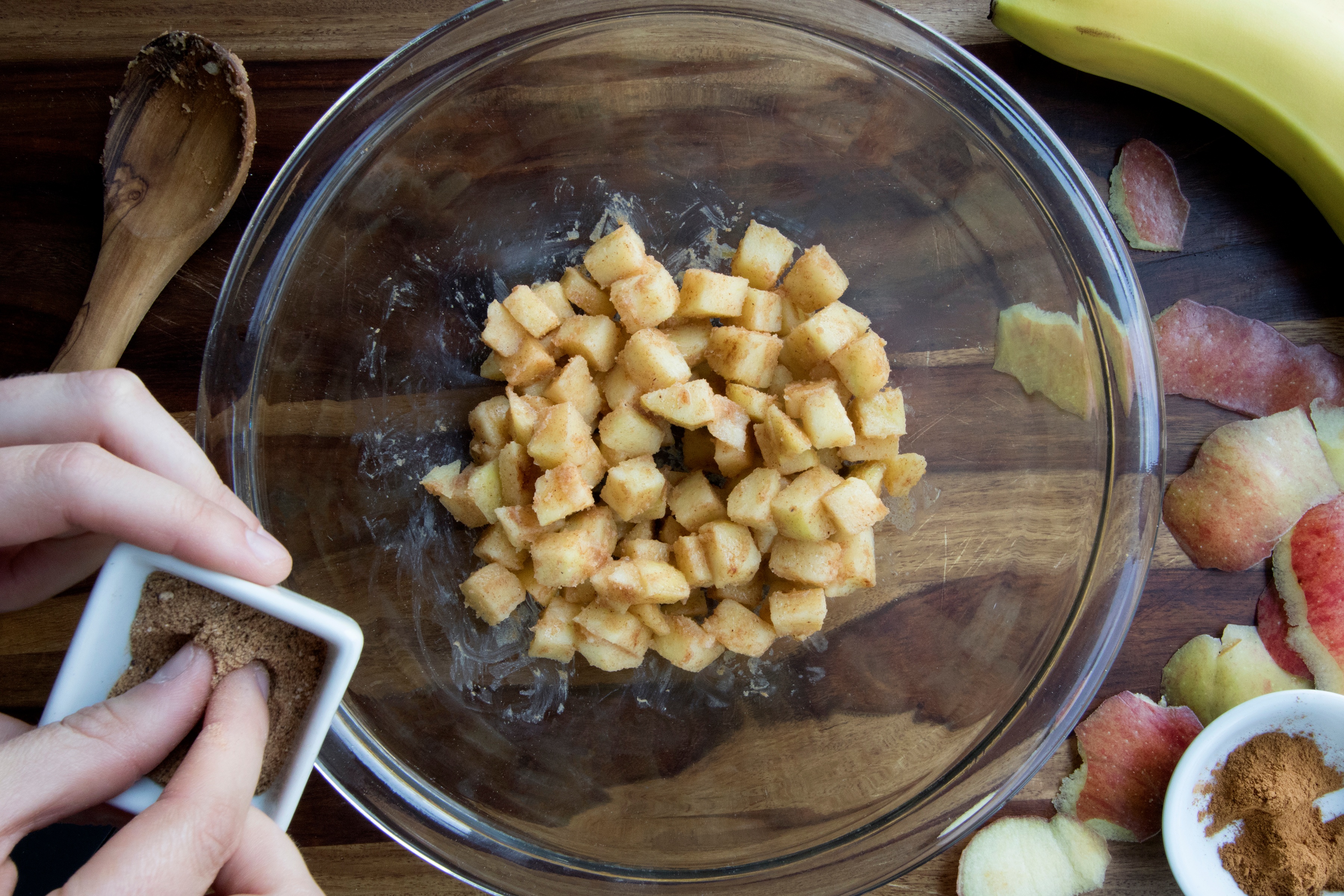 Hand pinching a small amount of spice to add to bowl of seasoned cut apples in glass bowl