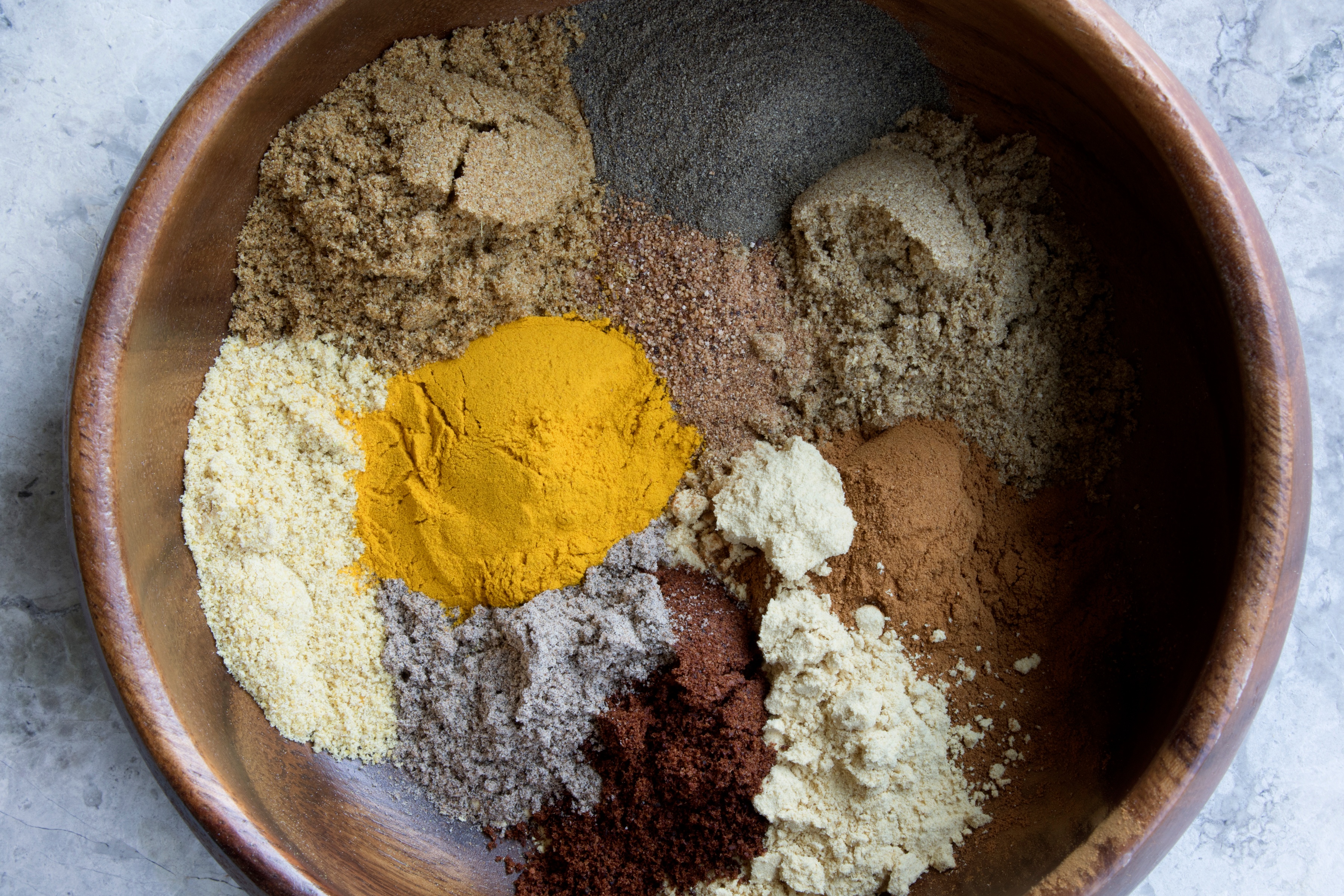 Wooden bowl filled with vibrant colored powdered herbs and spices