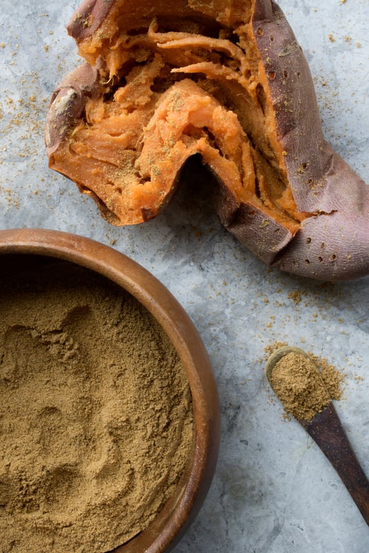 Artistic picture of baked and opened sweet potato with bowl of curry spice blend powder and spoon with same powder. 