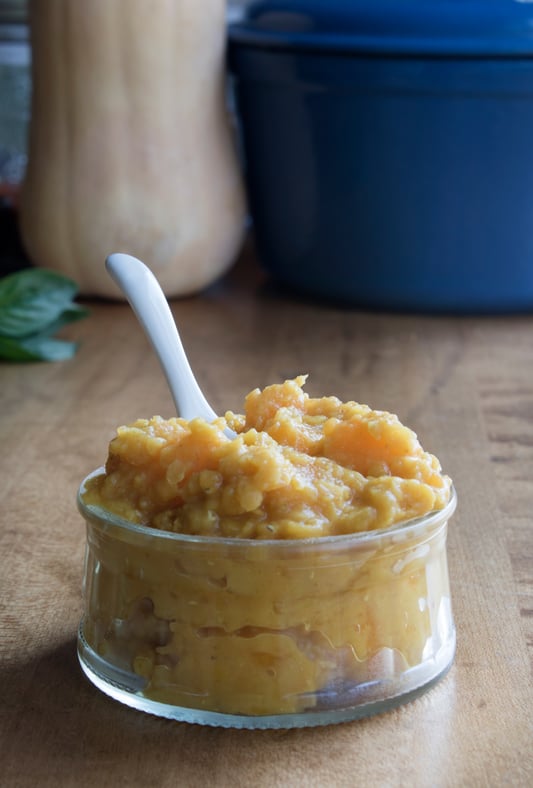 Glass jar of homemade baby food recipe with small spoon on wooden table