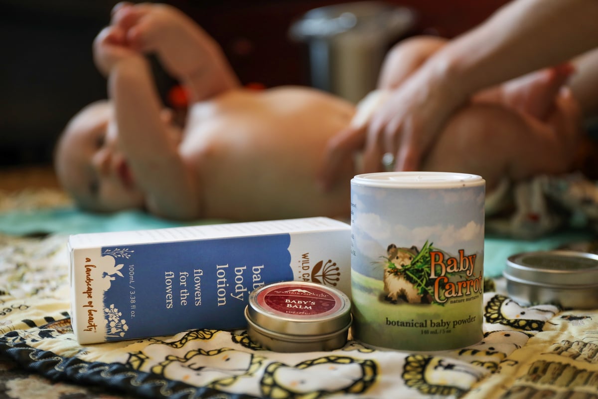 Natural baby products on blanket with baby being changed in background.