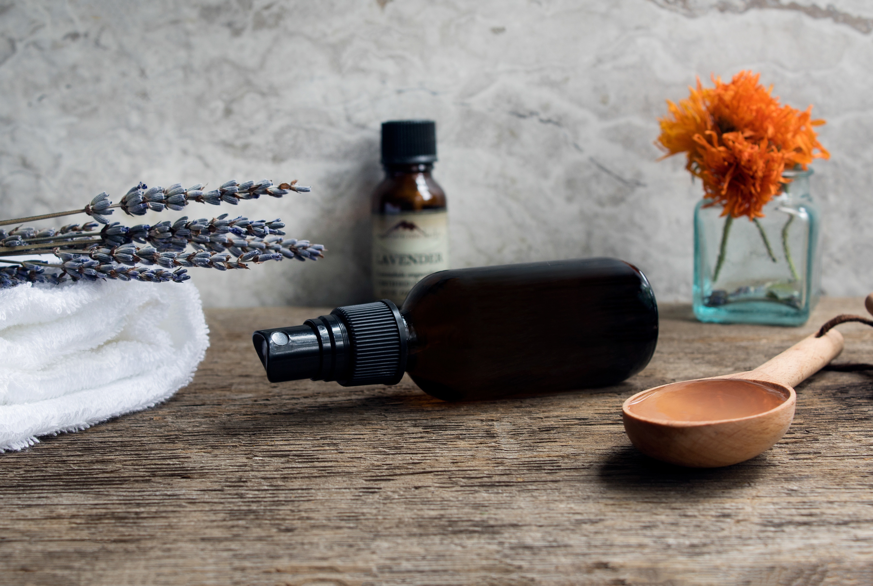 Small mister bottle laying on side on wooden surface next to wooden spoon and lavender