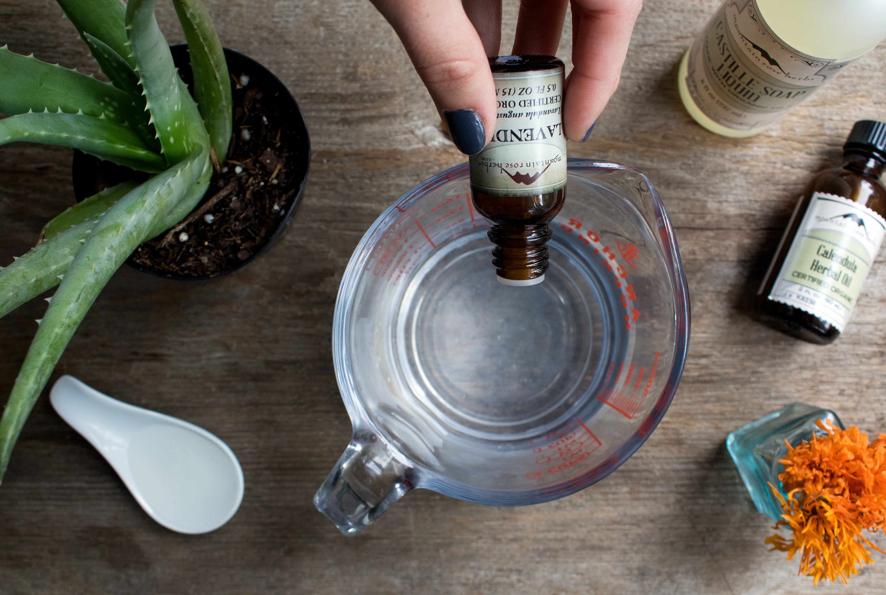 Hand holding lavender essential oil dripping it into measuring cup to make DIY baby wipe spray