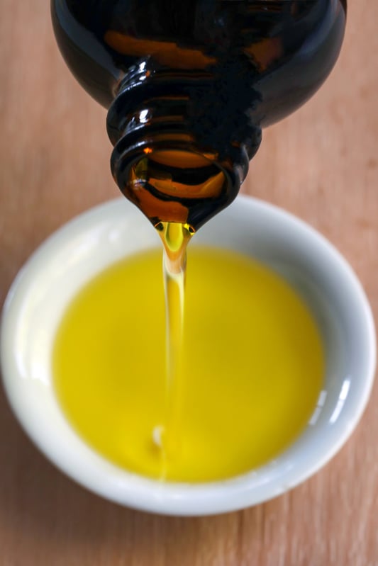 Amber glass bottle of organic baobab oil being poured into white ceramic dish