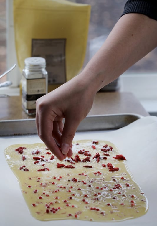 Hand sprinkling toppings on top of cooling homemade white chocolate bark.