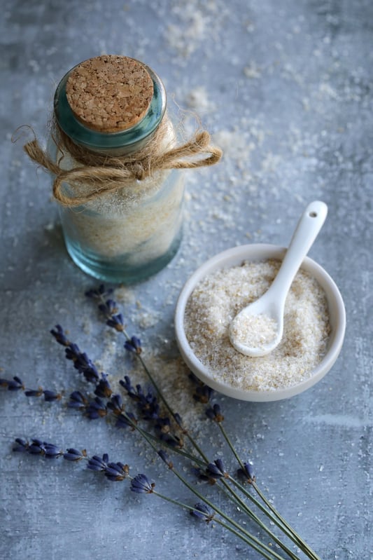 Decorative glass bottle with cork top and hemp rope and bow. White bowl of salt mixture with spoon in it.