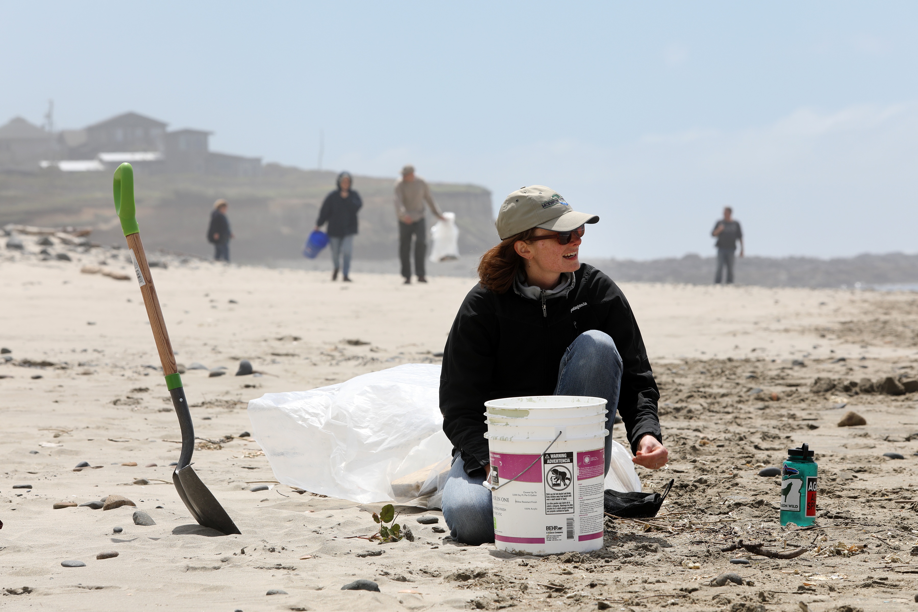 Woman on beach cleaning up trash with volunteer team