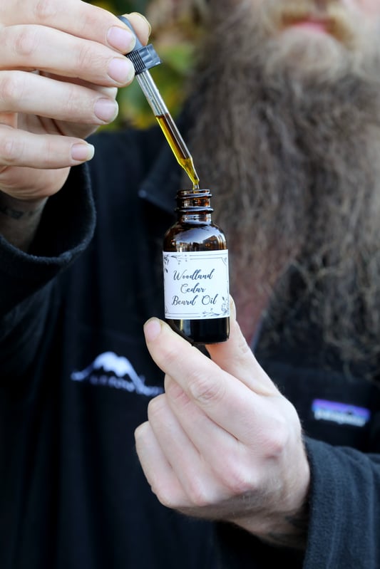 Man's hand using dropper top to display oil with long beard in background. 