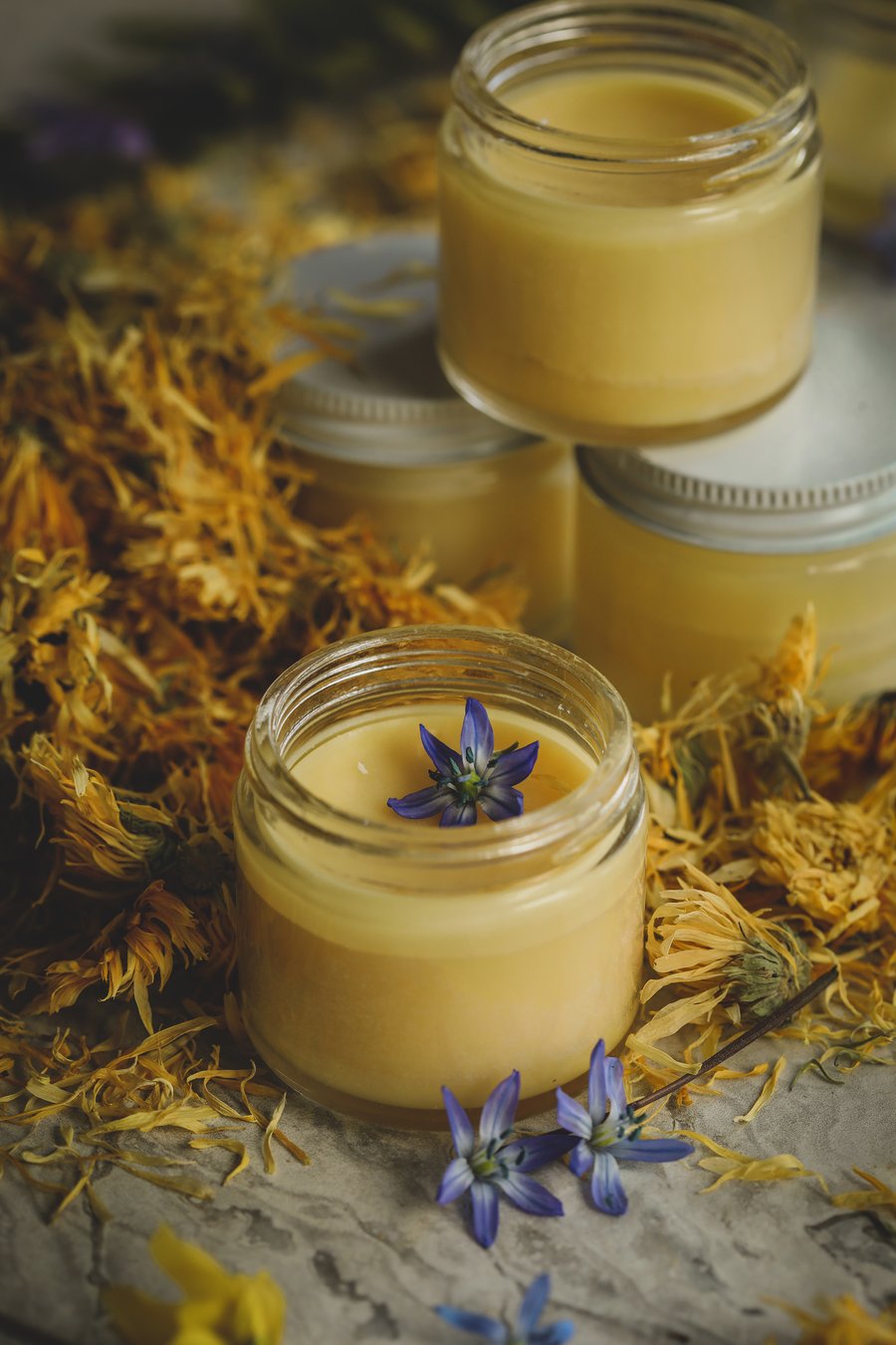 Homemade belly butter in jars amidst calendula flowers.