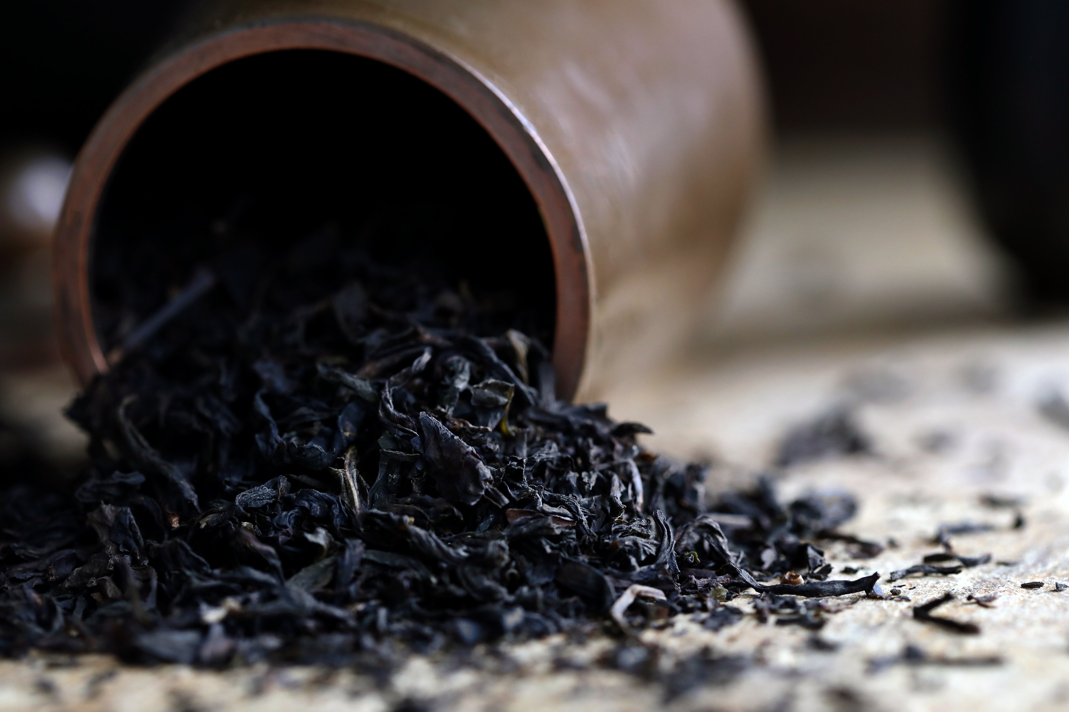 Dried black tea leaves pouring out of a wooden cylinder tea container.