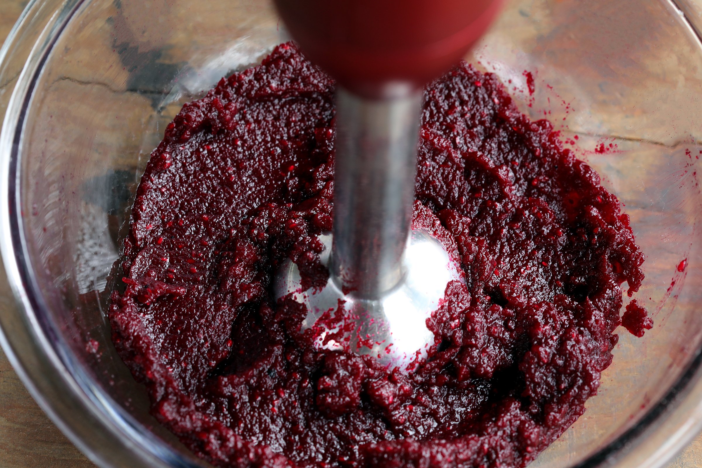 Immersion blender mixing deep red beet and chia paste in a clear glass bowl. 