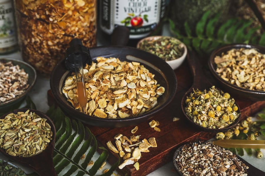 A smattering of bowls with dried aromatic and bitter herbs on a cutting board