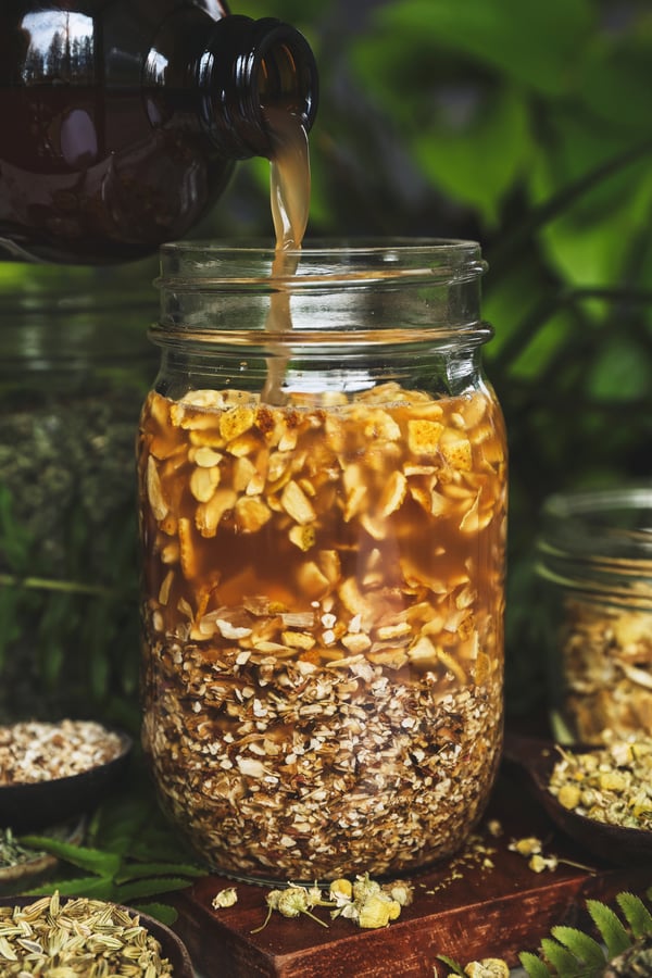 A jar filled with orange peel and dandelion root with vinegar being poured into it