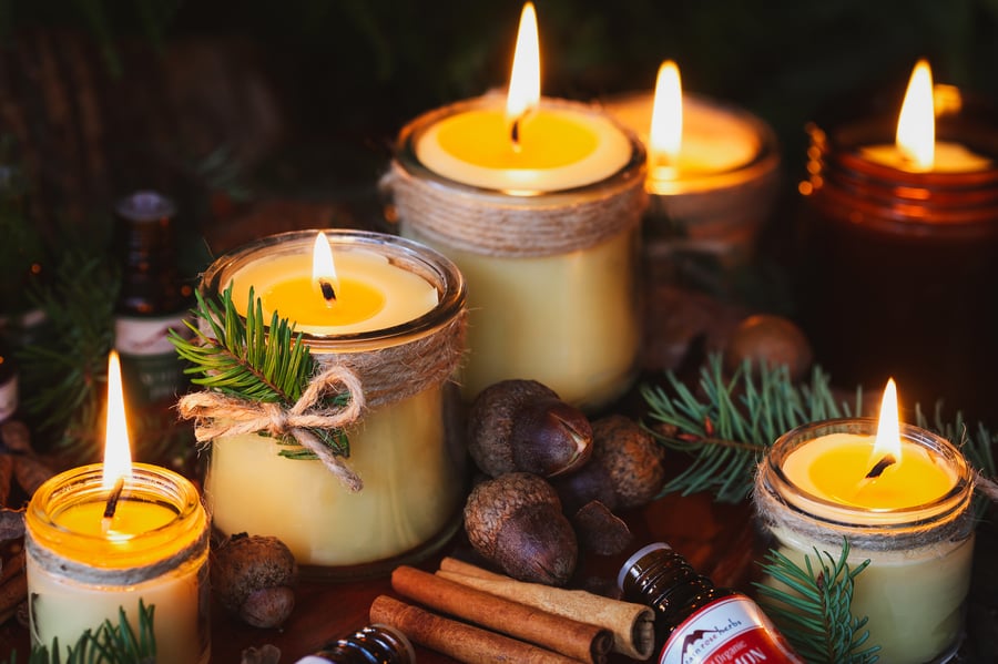 Various beeswax candles in jars all alight surrounded with acorns and leaves