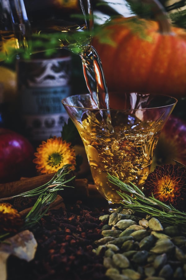 Golden apple cider being pouted into glass, surrounded by spices. 