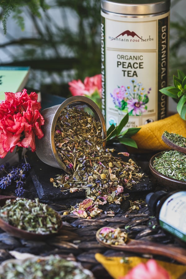 A tea strainer with peace tea and other herbs to support stress around it 