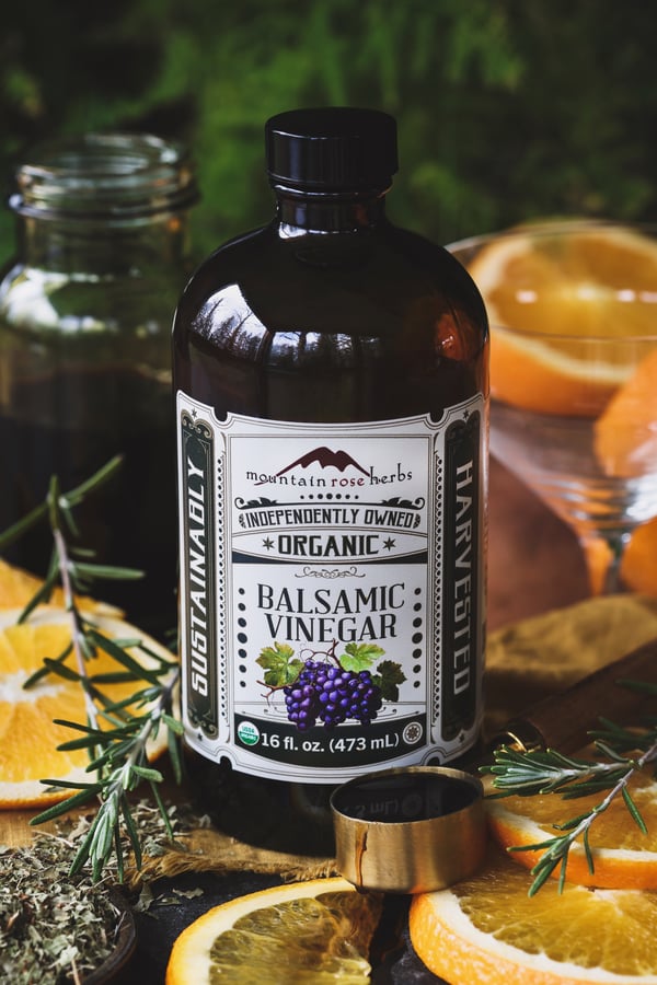 A jar of Mountain Rose Herbs' organic balsamic vinegar with fresh rosemary and orange slices around it