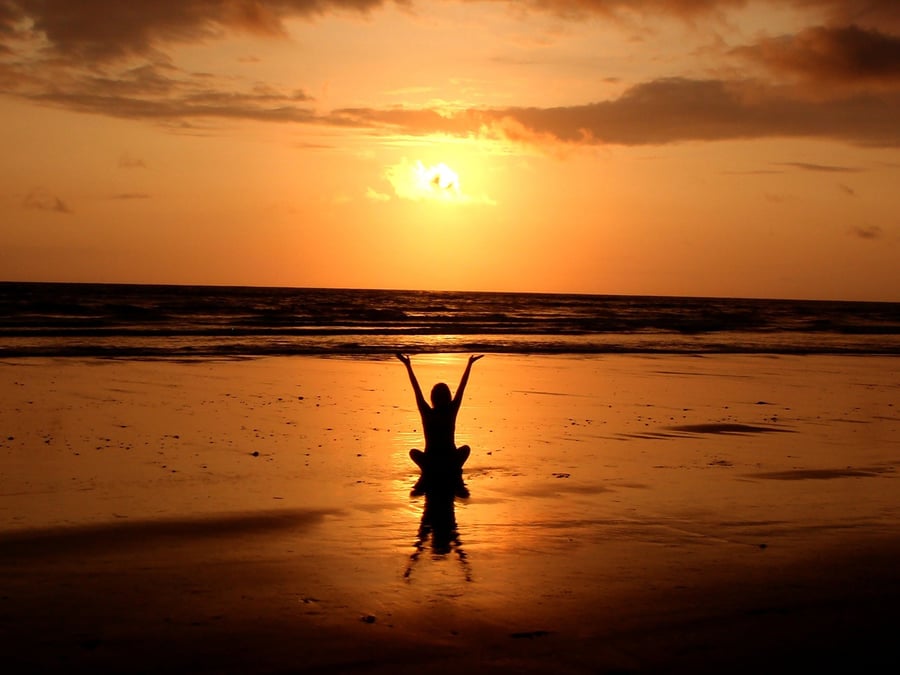 Someone practicing yoga on the beach at sunset