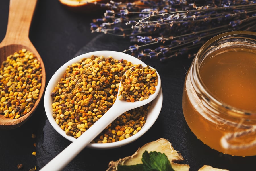 A small bowl of bee pollen near some honey and lavender
