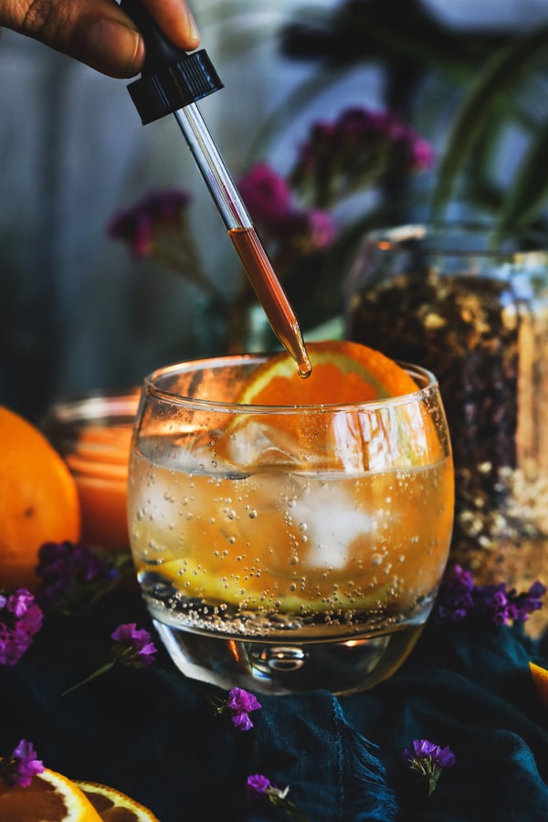 A dropper of herbal bitters is added to a cup of fizzy water and juice