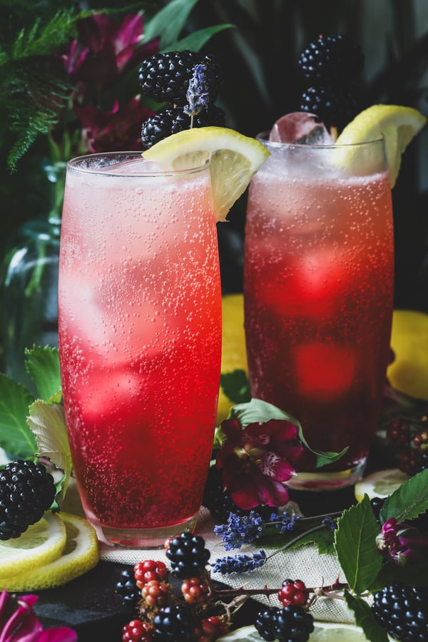 Two frosty blackberry lavender mocktails sit out garnished with blackberries and lemon