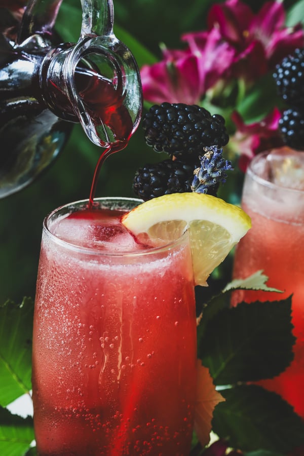 Blackberry lavender simple syrup is poured into an icy mocktail