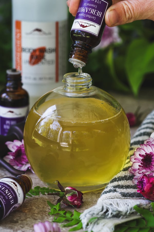 Bergamot essential oil being dripped into a soap dispenser filled with body wash base