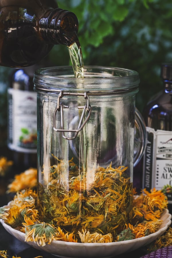 Oil being poured into a jar of dried calendula flowers