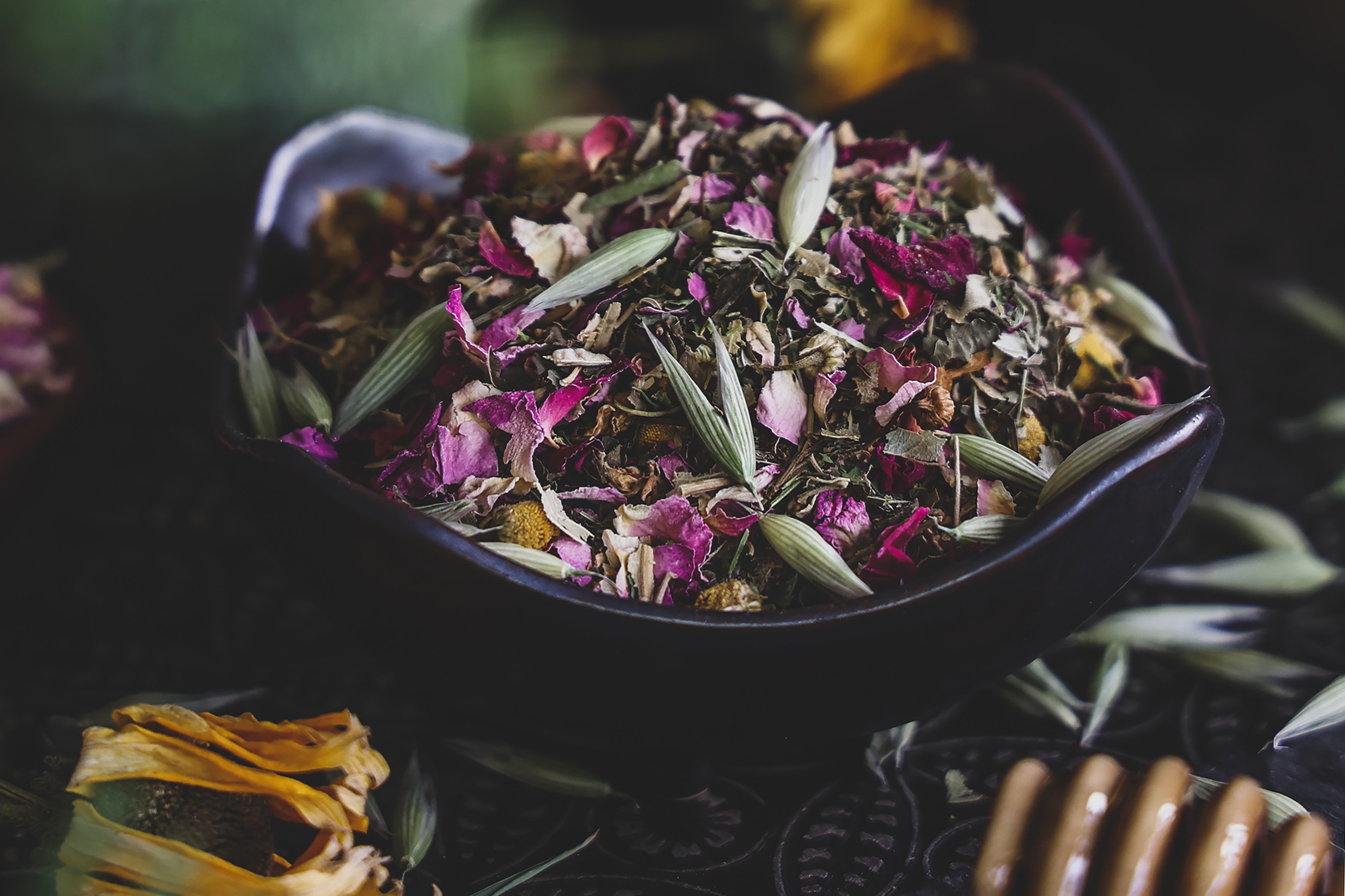 Bowl of colorful herbs including rose petals, oat tops, and chamomile flowers. 