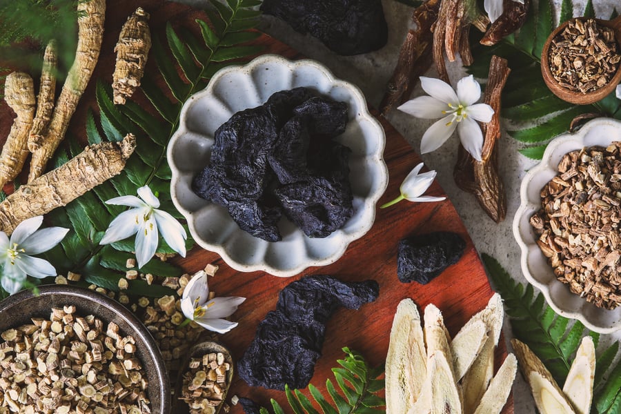 The tonic herbs used in Chinese Medicine sitting in bowls with ferns and flowers around them