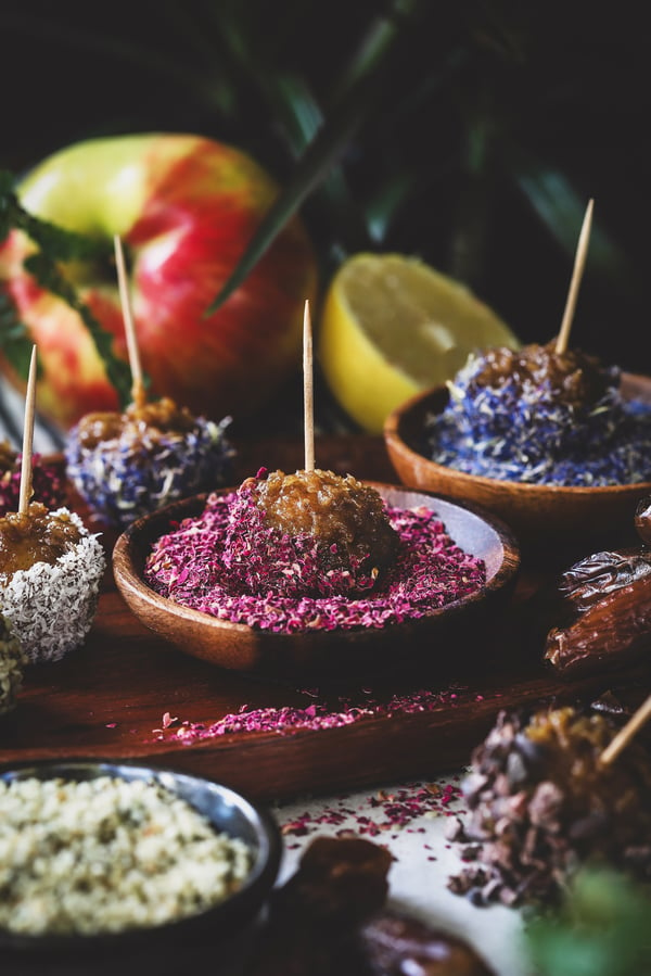 A caramel apple bite is dipped into a bowl of ground up rose petals