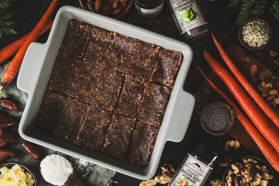 A dish of cut carrot cake bars sits on a counter surrounded with ingredients