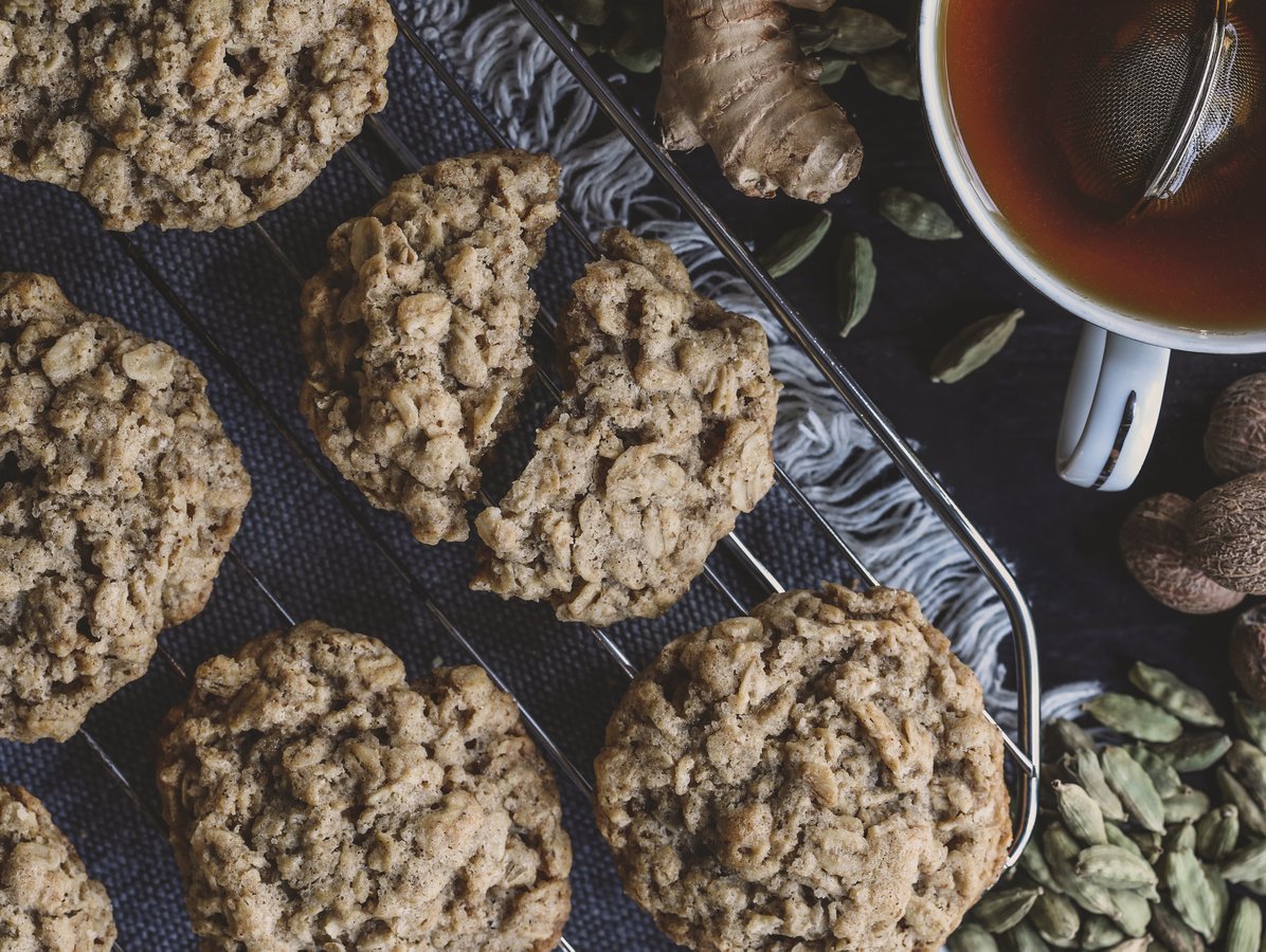 Chai spice oatmeal cookies on a rack next to a cup of tea and whole spices.