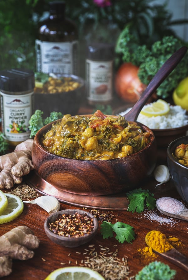 A bowl of steamy chickpea curry with spices and ingredients around it