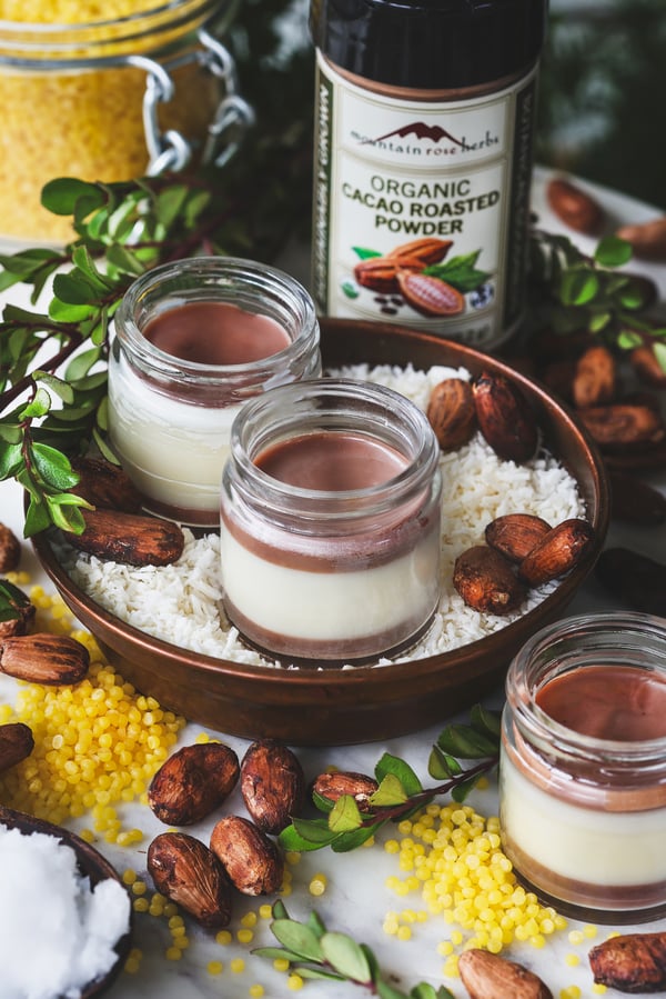 Jars of chocolate macaroon lip balm sits in small bowl with coconut flakes and other ingredients around it